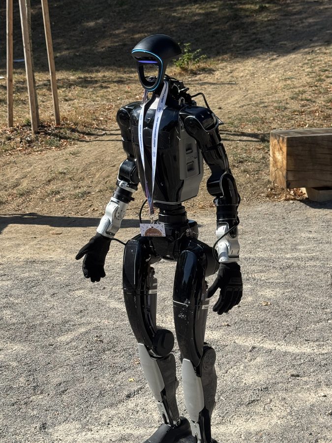 Čierny humanoidný robot Unitree G1 kráča po štrkovej ceste na vonkajšej akcii