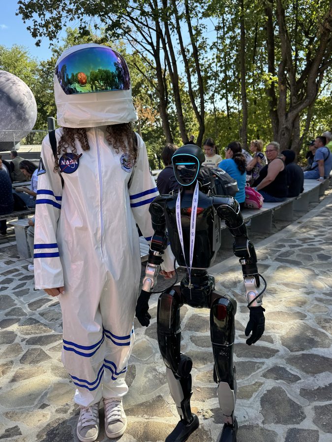 A child in an astronaut suit holding hands with a humanoid robot at a festival