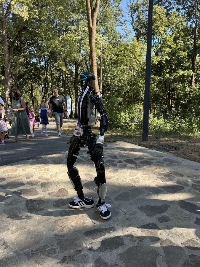 Humanoid robot walking along the stone path of an amphitheatre at a summer festival, surrounded by visitors